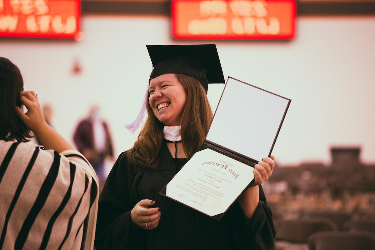 一名丹麦大学生身穿传统长袍，头戴帽子，手持毕业证书，在毕业典礼上摆姿势微笑.